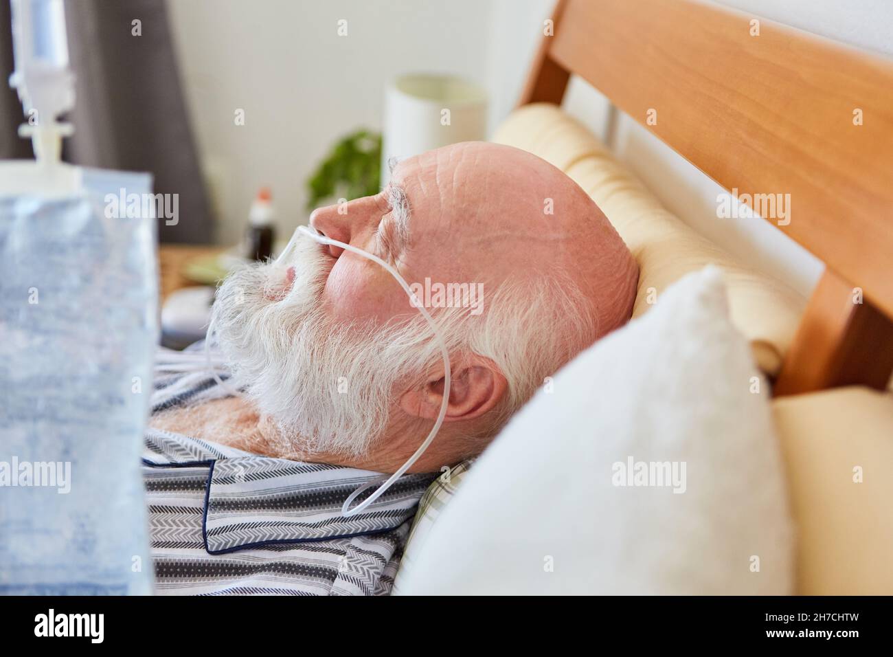 Kranker Senior mit Nasenkanüle während der Sauerstoffbehandlung und mit Infusionsbeutel im Vordergrund Stockfoto