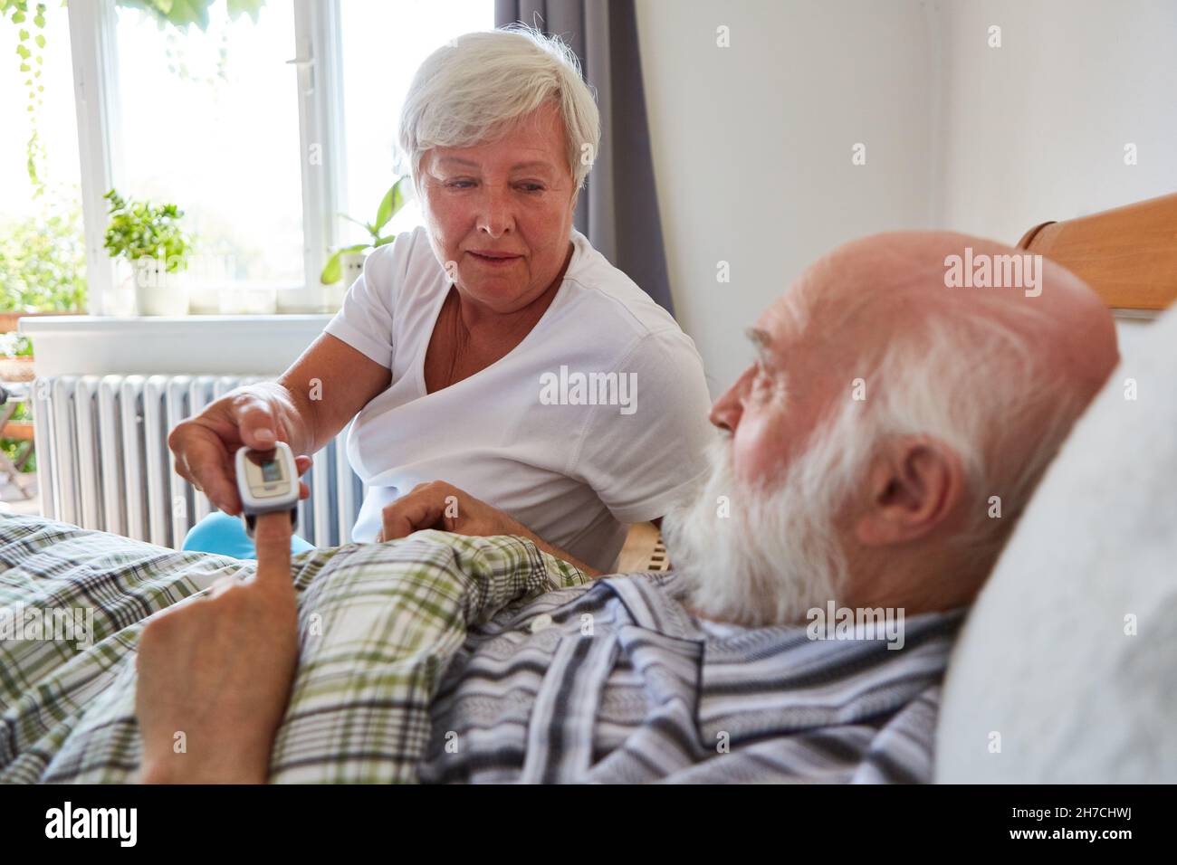 Die geriatrische Krankenschwester misst den Puls von kranken Senioren im Bett mit einem Pulsoximeter in der häuslichen Pflege Stockfoto