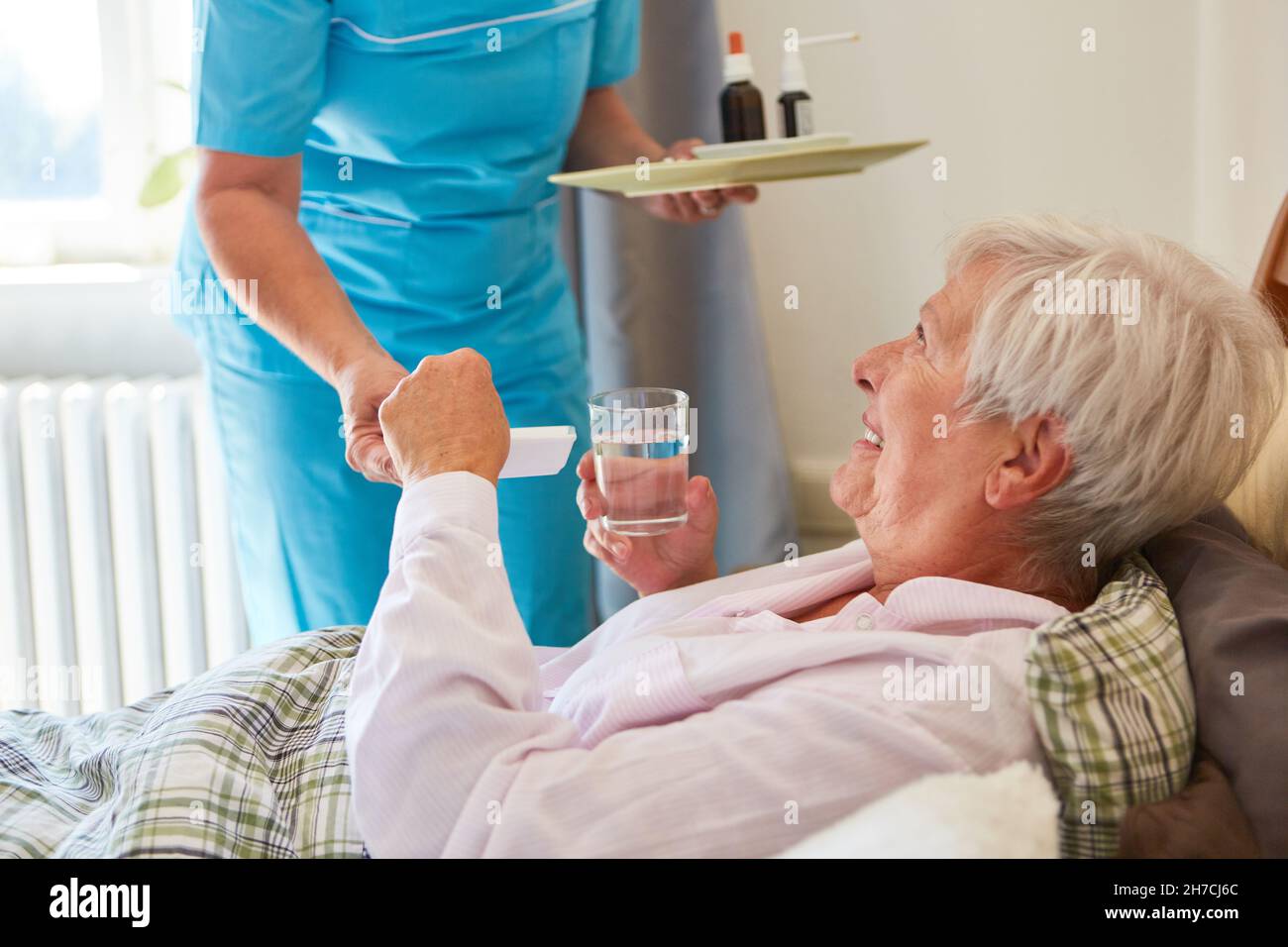 Die Pflegekraft gibt der alten Frau als Patientin zu Hause im Bett Pillen Stockfoto