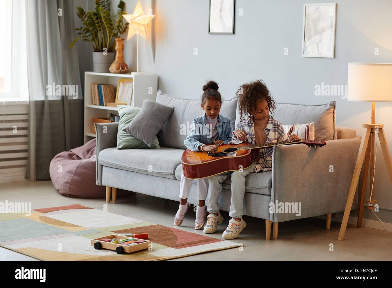 In voller Länge Porträt von zwei niedlichen Mädchen spielen mit akustischen Gitarre in gemütlichen Zuhause Interieur, kopieren Raum Stockfoto