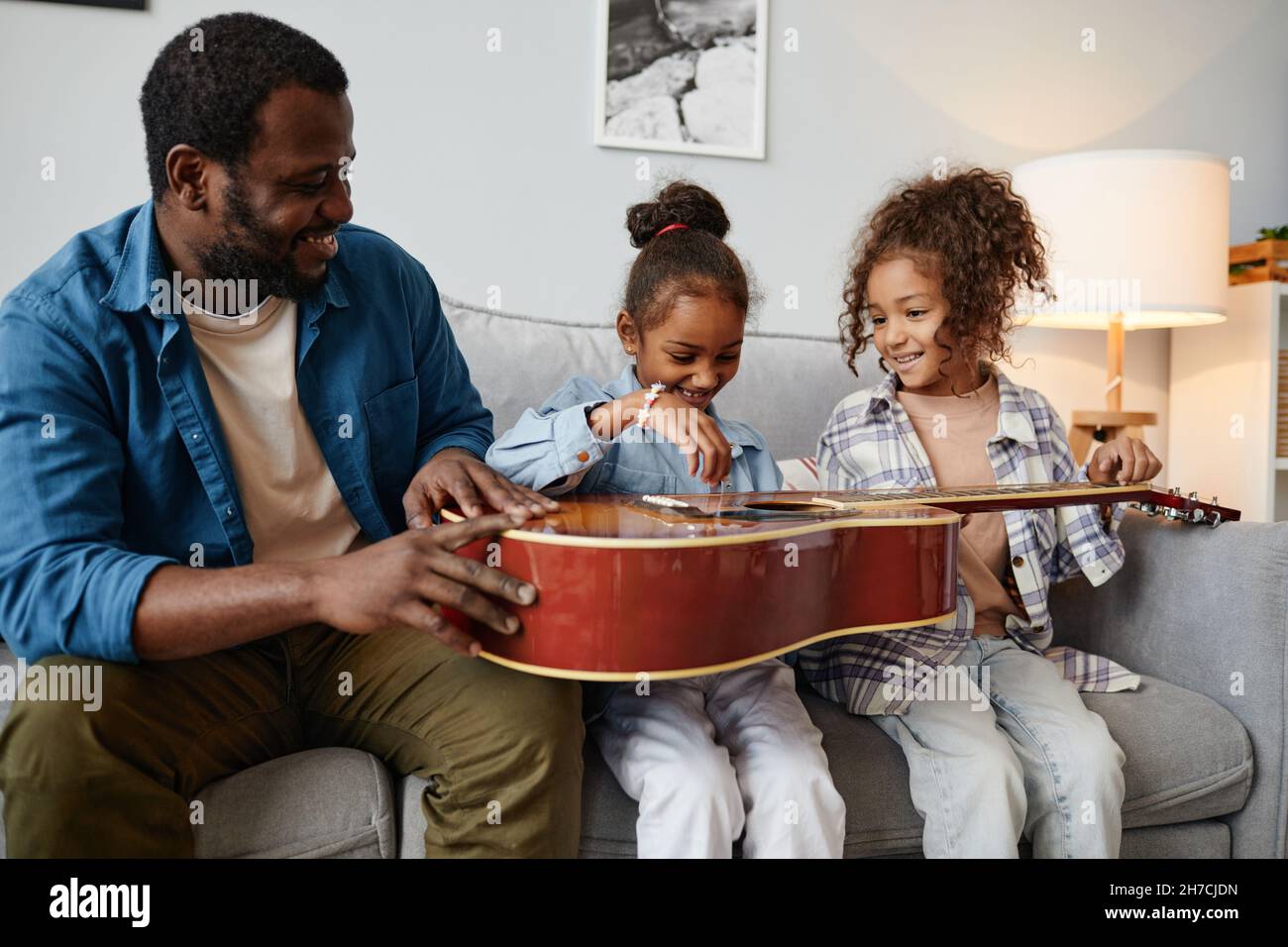 Porträt eines glücklichen afroamerikanischen Vaters, der mit zwei niedlichen Mädchen zu Hause spielt Stockfoto