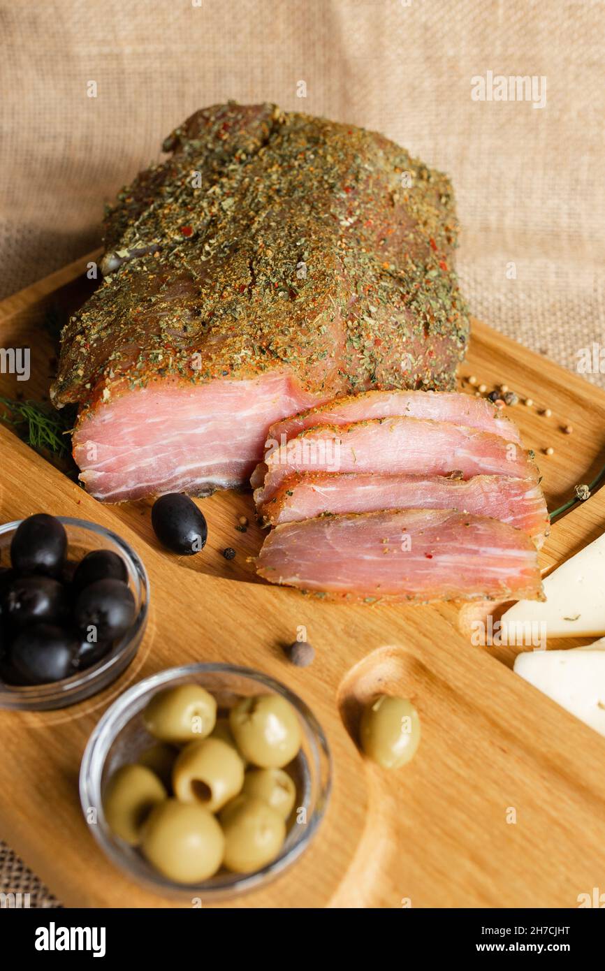 Getrocknete Schweinsfilet auf dem hölzernen Servierbrett mit Käse, Oliven, schwarzem Pfeffer, Tomatensauce. Jerky Filet Vorspeise. Gericht von Weißrussisch Stockfoto