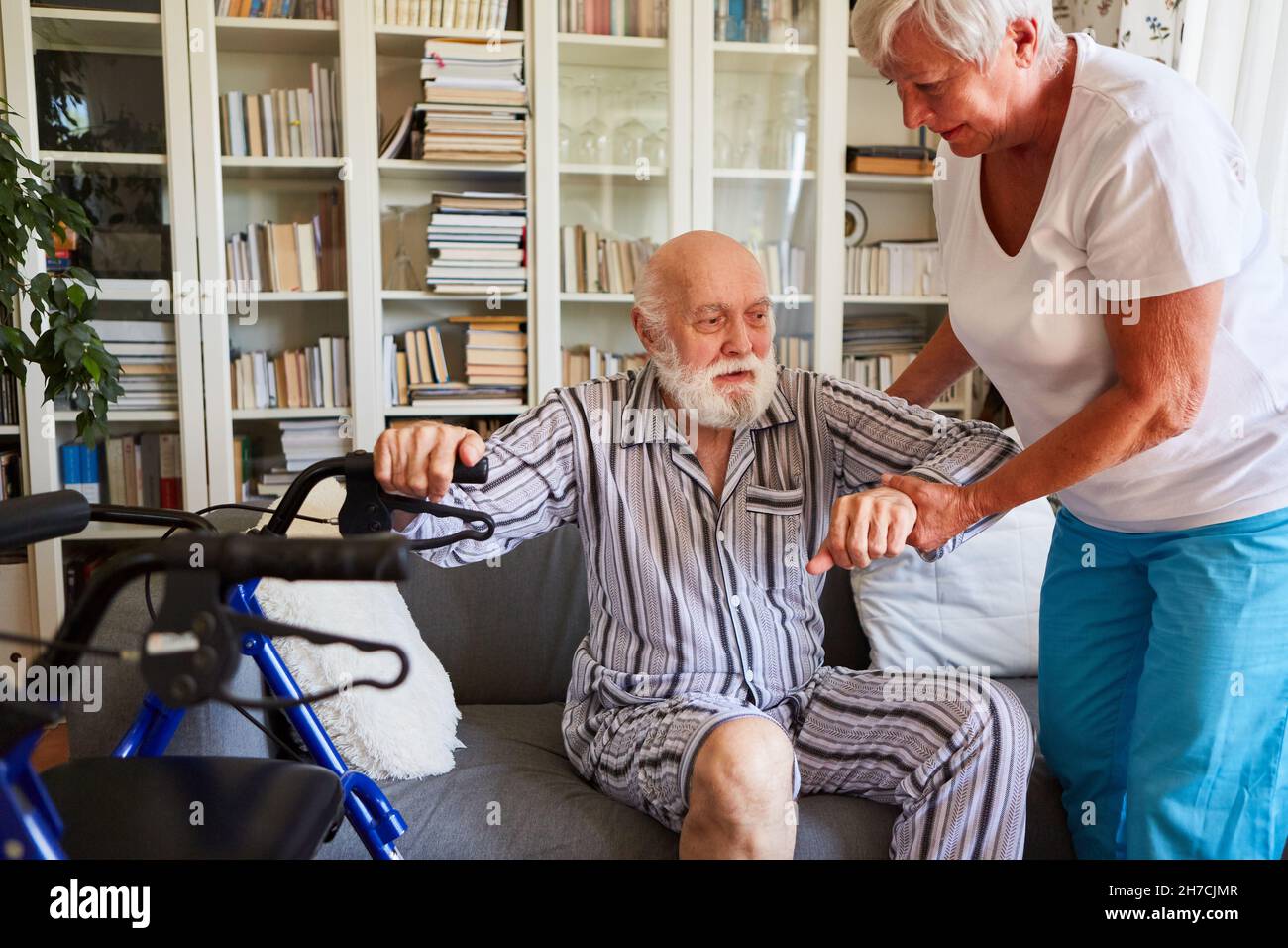 Ältere Pflegekraft hilft Senioren mit Rollator, vom Sofa zu Hause aufzustehen Stockfoto