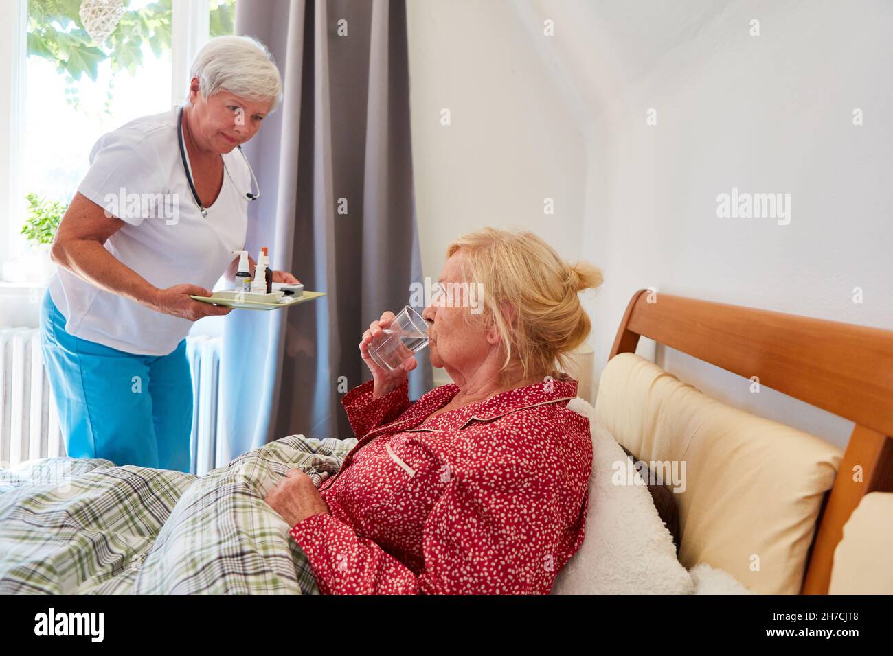 Pflegekraft Frau verteilt Medikamente an kranke ältere Frau im Bett zu Hause oder im Altersheim Stockfoto