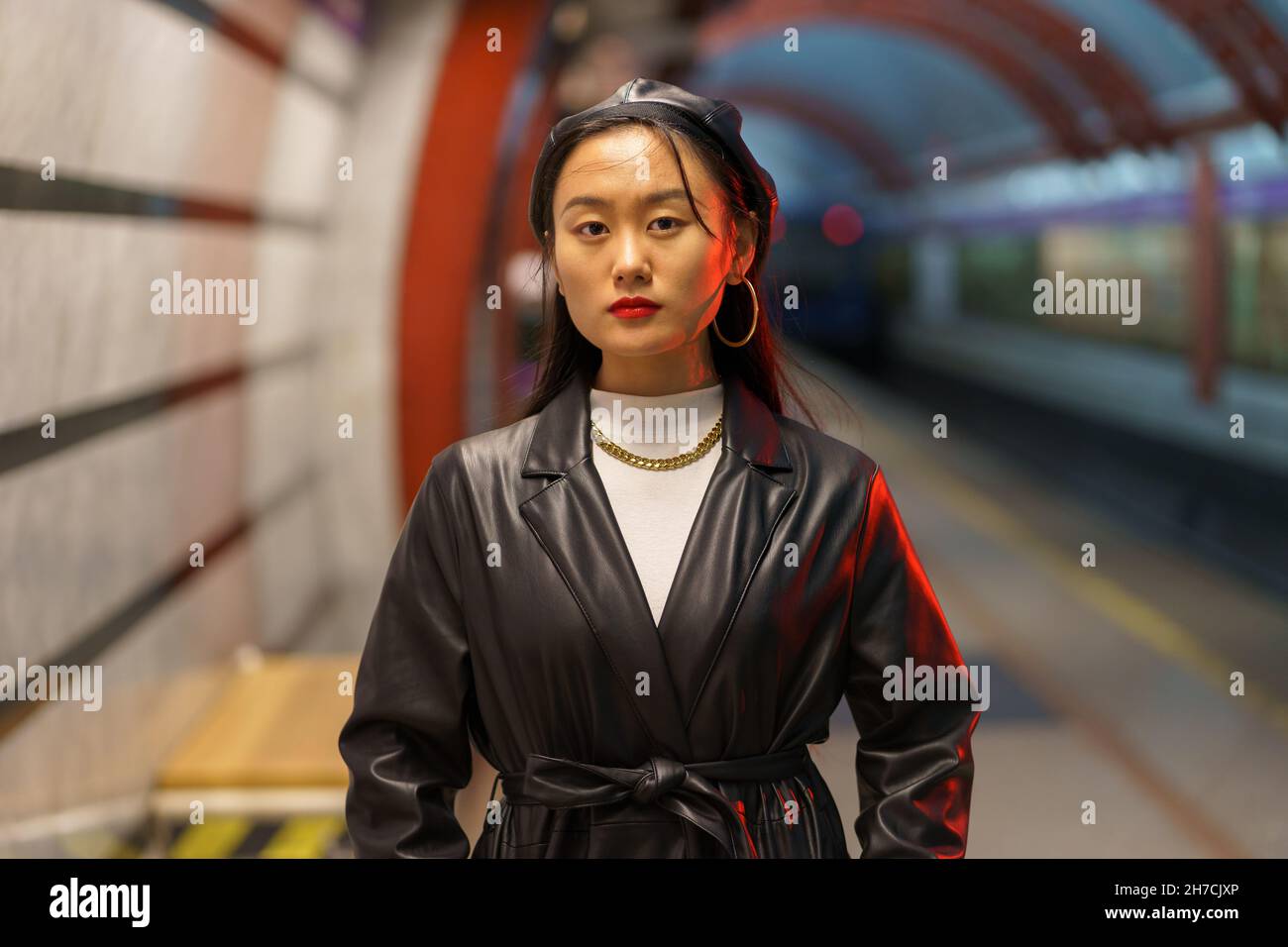 Stilvolle asiatische Mädchen in Leder Baskenmütze und Trenchcoat warten auf Zug an U-Bahn-Station Stockfoto