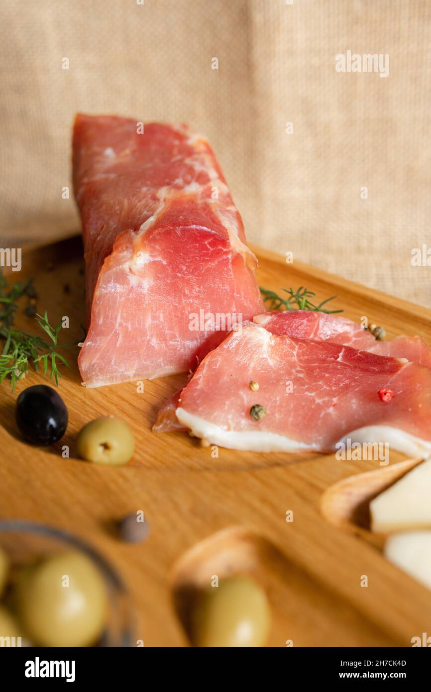 Getrocknete Schweinsfilet auf dem hölzernen Servierbrett mit Käse, Oliven, schwarzem Pfeffer, Tomatensauce. Jerky Filet Vorspeise. Gericht von Weißrussisch Stockfoto