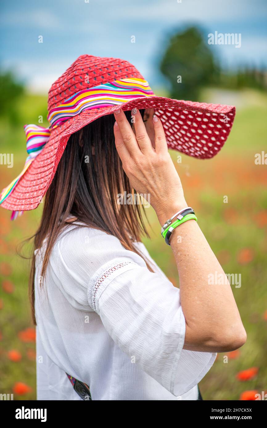 Schöne Frau trägt Strohhut genießen den Blick auf eine Mohnwiese im Frühjahr Saison Stockfoto