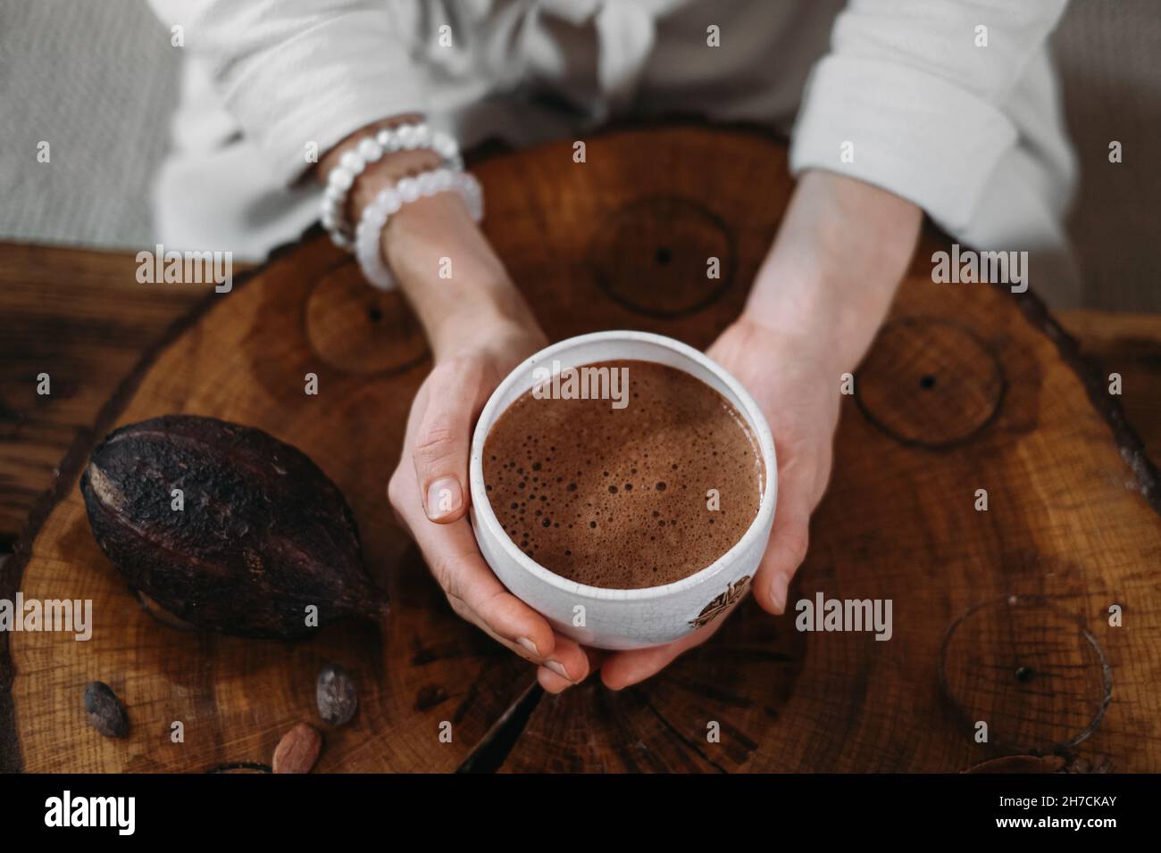 Heißer handgemachter zeremonieller Kakao in weißer Tasse. Frau Hände halten Handwerk Kakao, Draufsicht auf Holztisch. Bio gesundes Schokoladengetränk aus zubereitet Stockfoto