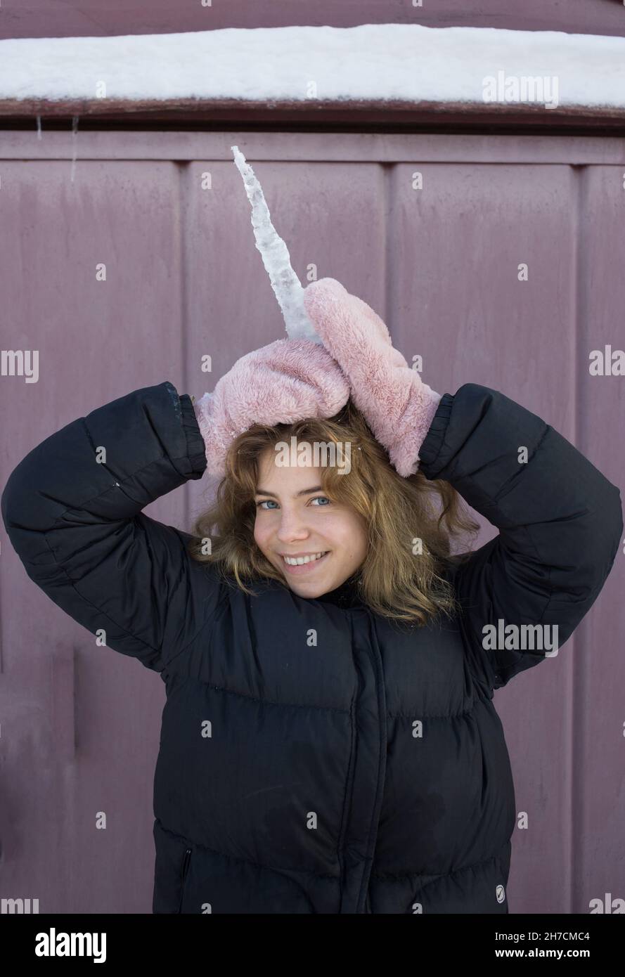 Porträt eines niedlichen Teenagers von 16-17 Jahren, das mit einem großen durchsichtigen Eiszapfen spielt und es wie ein Einhorn am Kopf hält. Fröhlicher Wint Stockfoto