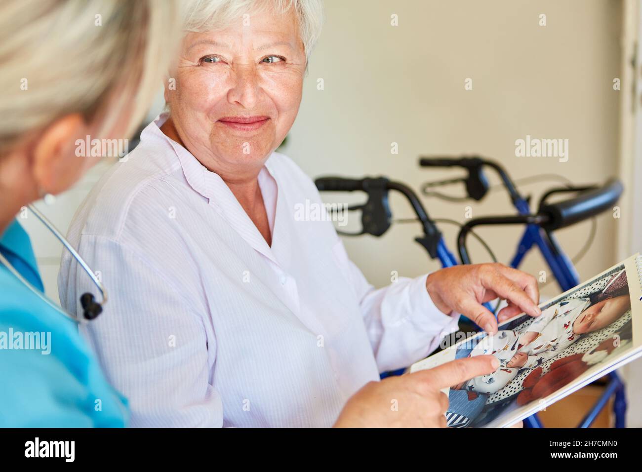 Lächelnde alte Frau mit Demenz und geriatrische Krankenschwester Blick auf Kalender mit Baby-Foto Stockfoto