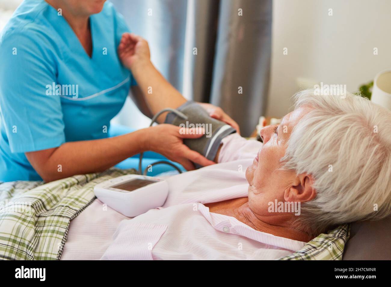 Eine Frau aus dem Pflegedienst, die den Blutdruck eines älteren Bürgers als Patientin im Bett zu Hause misst Stockfoto