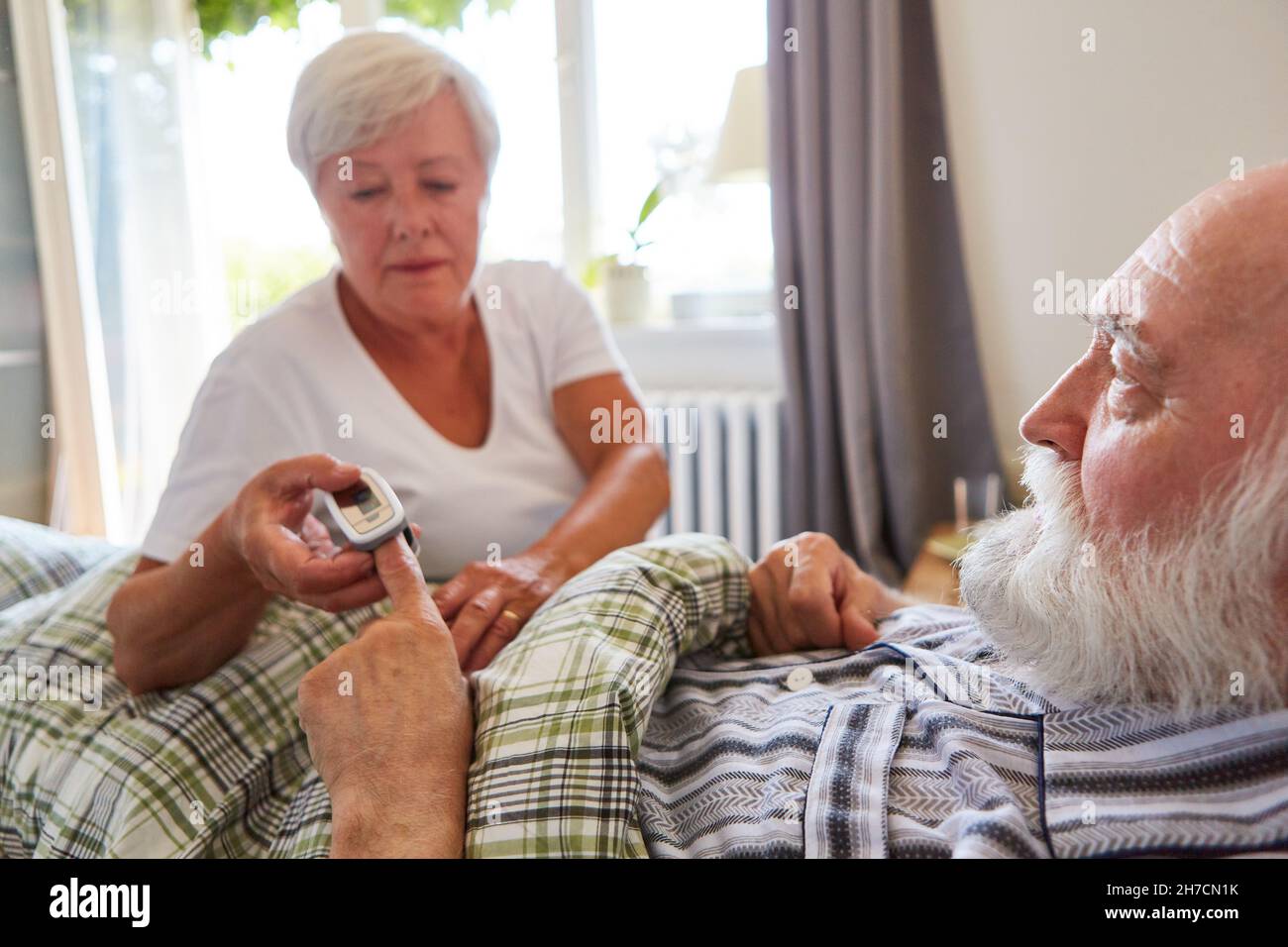 Die Pflegekraft überprüft den Puls des Seniorinnen im Bett mit dem Pulsoximeter im Pflegeheim Stockfoto
