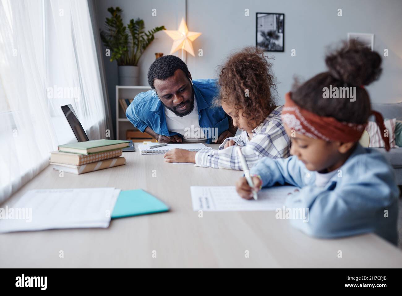 Porträt eines fürsorglichen Vaters, der Hausaufgaben mit zwei kleinen Mädchen zu Hause macht, Platz kopieren Stockfoto