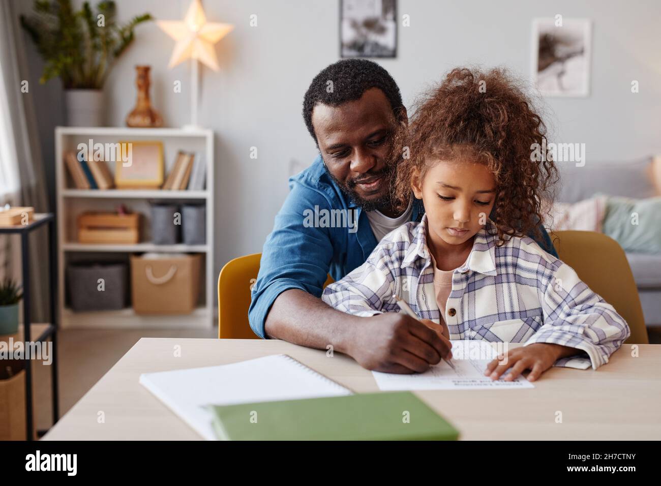 Porträt eines fürsorglichen afroamerikanischen Vaters, der Hausaufgaben mit seiner Tochter zu Hause macht, Platz kopieren Stockfoto