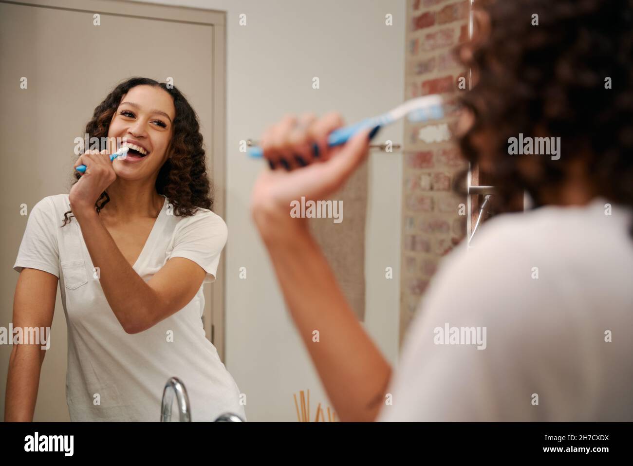 Gesunde multikulturelle junge Frau, die im Badezimmer als Mikrofon in die Zahnbürste singt. Glücklich, tanzen im modernen Badezimmer. Stockfoto