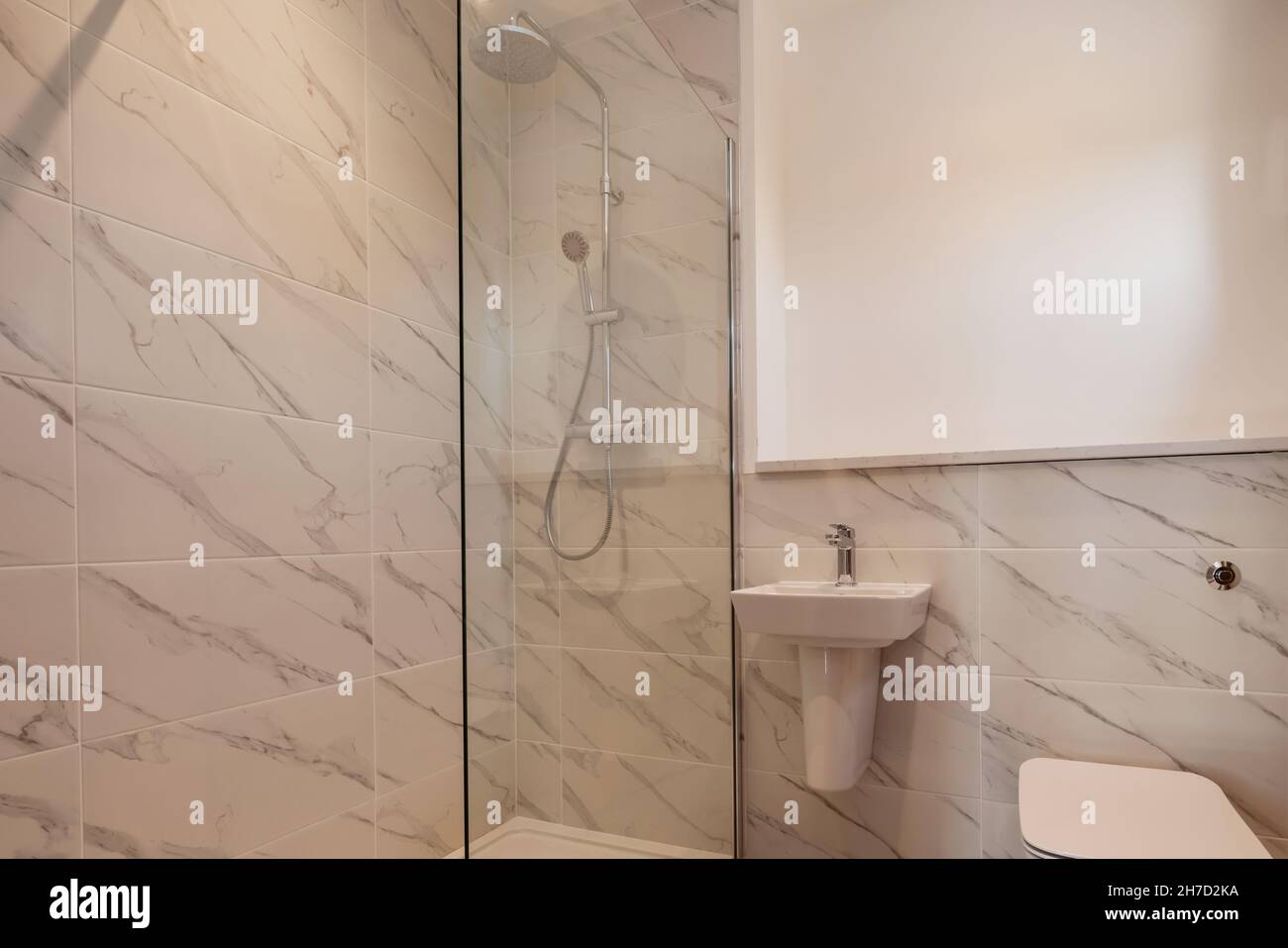 Generisches Duschbad mit Waschbecken und wc, teilweise geflieste Wände und Glasduschwand. Stockfoto