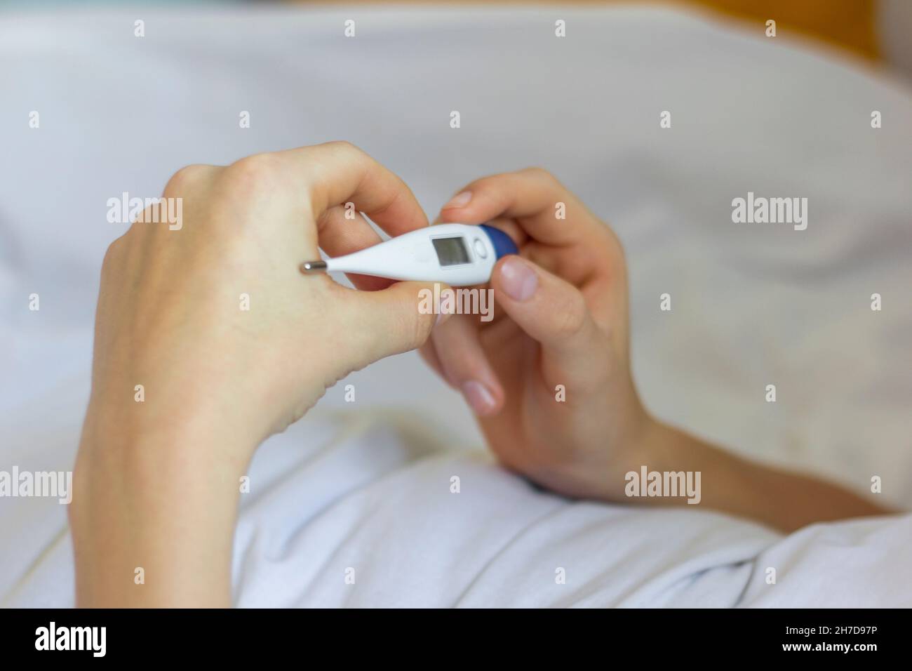 Ein kranker Mensch liegt mit einem Thermometer in den Händen im Bett Stockfoto