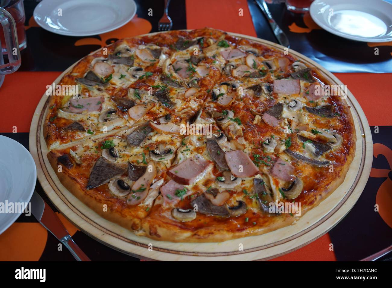 Eine riesige Pizza mit verschiedenen Füllungen steht auf einem roten Tisch, umgeben von weißem Geschirr Stockfoto