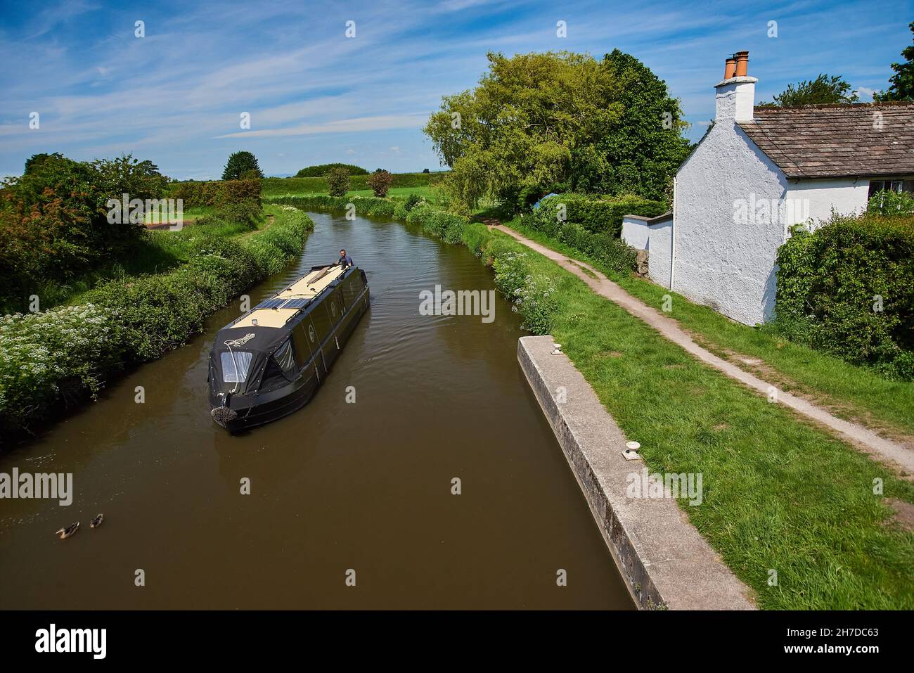 Ein Schmalboot, das an einem Haus am Kanal entlang am Rufford Branch des Leeds und Liverpool Kanals im Nordwesten Englands vorbeifährt Stockfoto