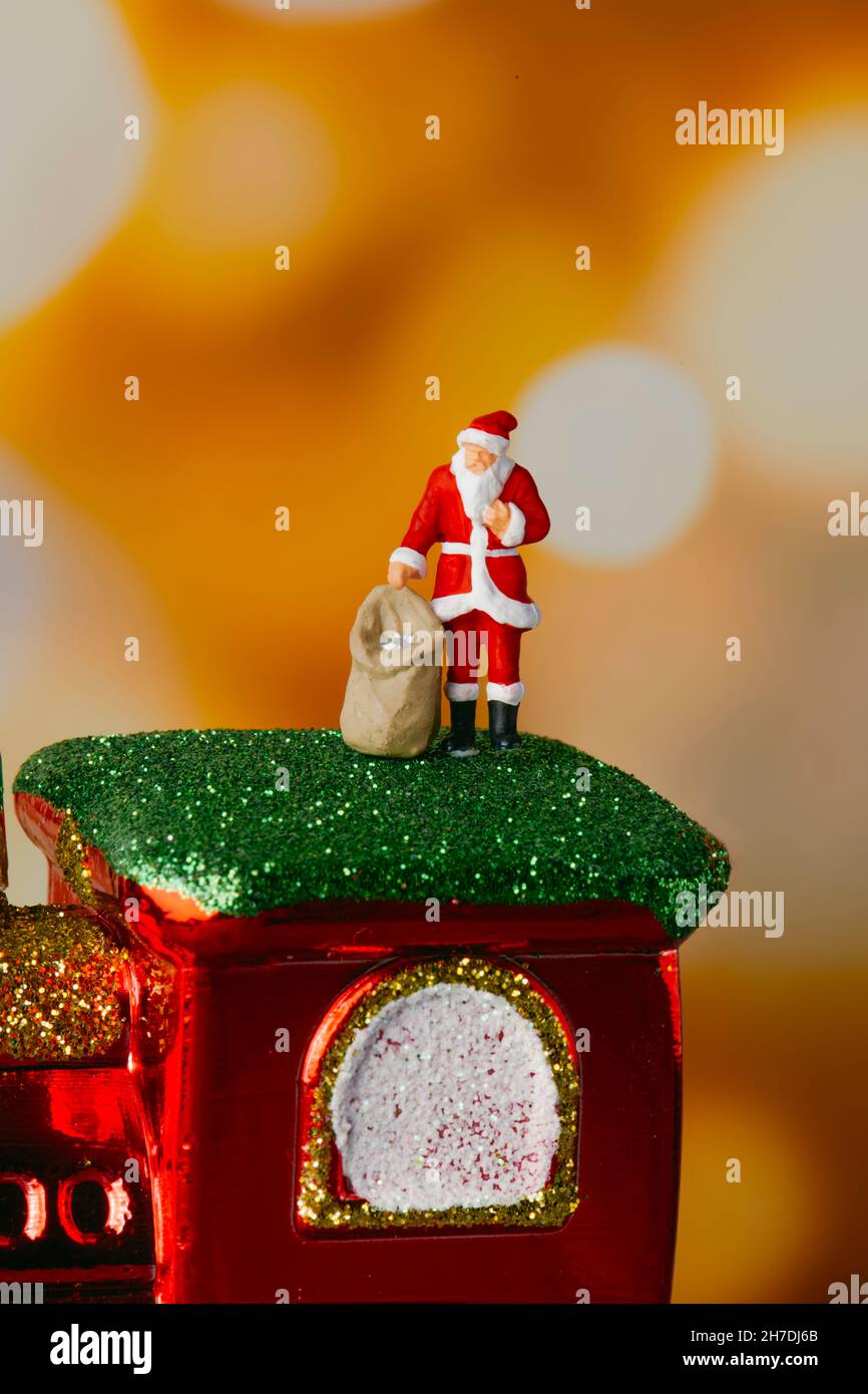 Nahaufnahme eines kleinen weihnachtsmanns, der einen Sack mit Geschenken trägt, der auf einer Spielzeuglokomotive auf einem Bokeh-Effekt-Hintergrund steht Stockfoto