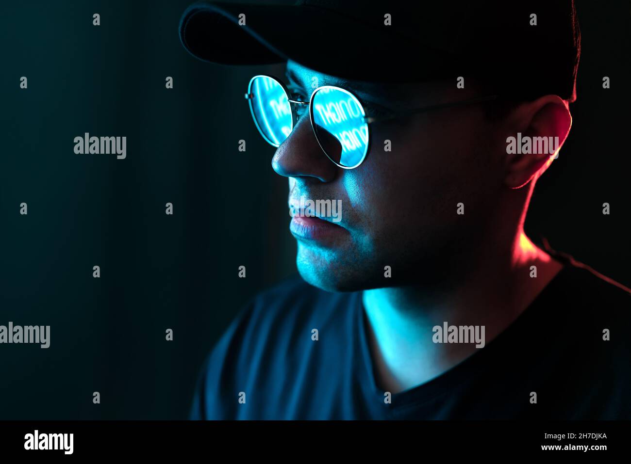 Mann mit Neonlicht auf Brille und Gesicht. Blaue und rote Farbe von der Stadt-Plakatwand im dunklen Studioportrait. Spiegelung in Sonnenbrillen. Schwarzer Hintergrund. Stockfoto