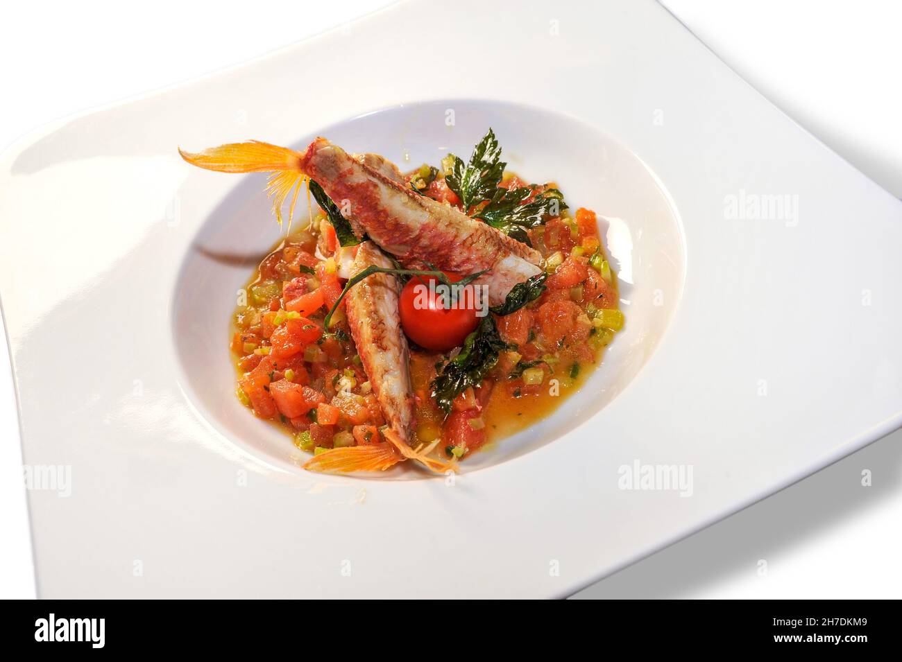 Goatfish oder Rote Meeräsche in Tomatensauce mit Petersilie in weißem Teller . Italienisches Fischrezept namens Triglie alla livornese. Isoliert auf Weiß Stockfoto
