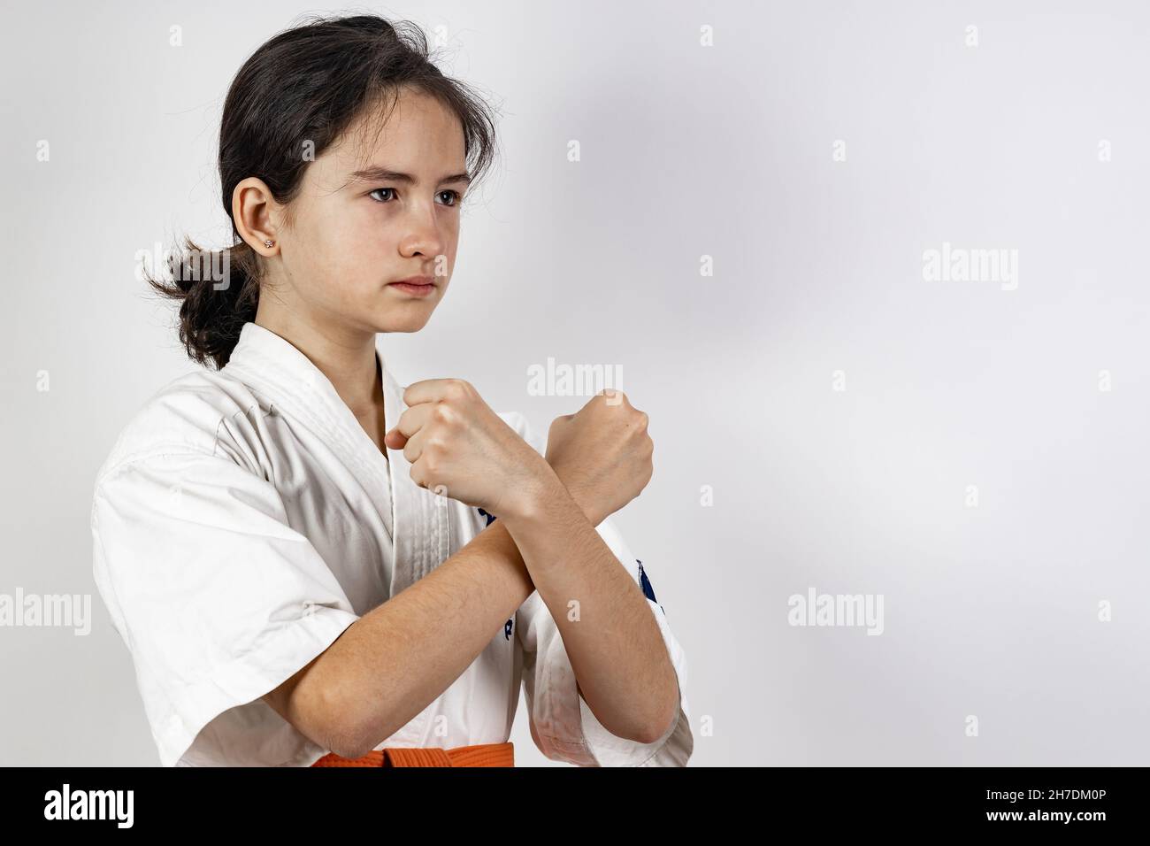 Karate Mädchen auf einem weißen Hintergrund. Sportliche kaukasische Brünette in einem weißen Kimono mit einem orangen Gürtel. Kontaktieren Sie den Sport. Orientalische Kampfkünste gesunde LIF Stockfoto