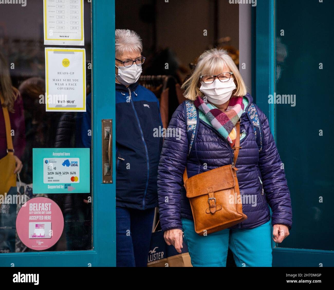 Zwei Frauen mit Gesichtsmasken verlassen das Geschäft White Stuff in Belfast, während sie an einem Schild vorbeigehen, auf dem alle Kunden darüber informiert werden, dass sie Gesichtsbezüge tragen müssen. Stockfoto