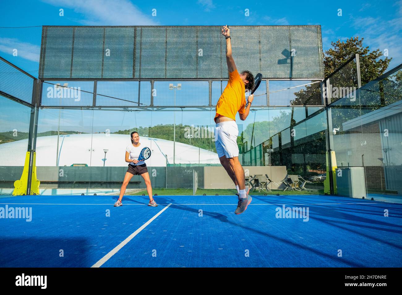 Gemischtes Padel-Match auf einem Padel-Platz mit blauem Gras - wunderschönes Mädchen und hübscher Mann, der im Freien Padel spielt Stockfoto