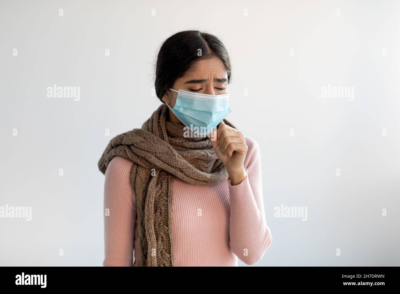 Verärgert verzweifelte junge indische Dame in Schutzmaske und Schal hustet, fühlt sich schlecht und leidet an Krankheit Stockfoto
