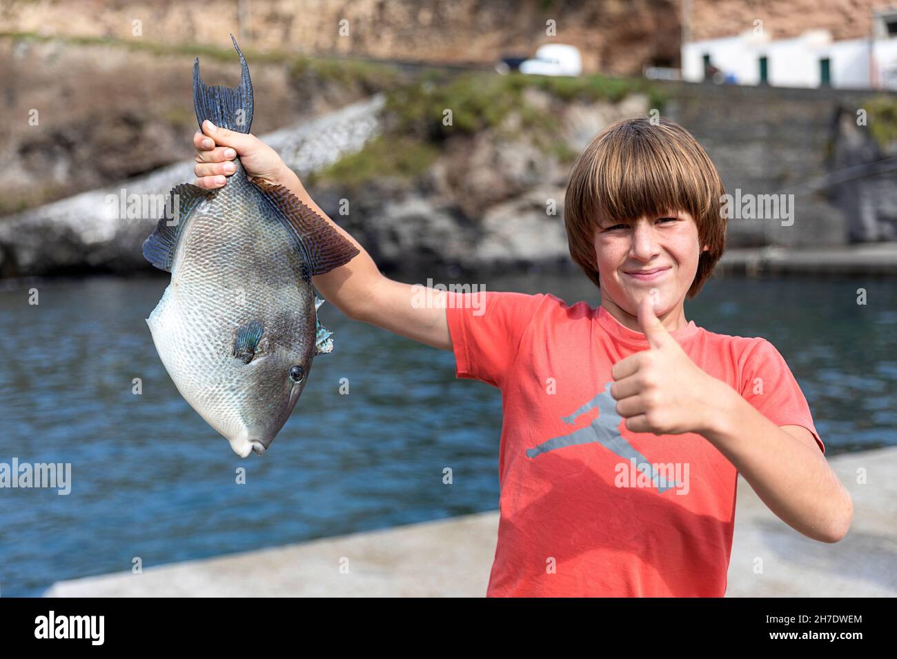 Der Junge hält stolz einen Triggerfisch (Balistidae), den er gerade vom Pier gefangen hat, Ponta Delgada, Flores, Azoren, Portugal, Europa Stockfoto