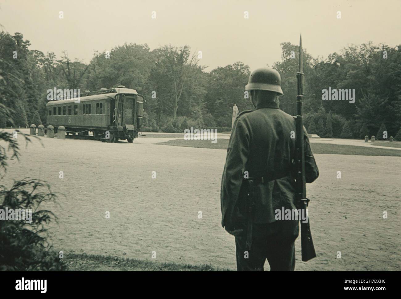 Deutscher Soldat stand neben dem Compiègne-Wagen des Marschalls Ferdinand Foch auf dem Boden der Waffenstillstandsglocke im Wald von Compiègne (Forêt de Compiègne) Im Juni 1940 wurde auf dem Gelände, wo der Waffenstillstand vom 11. November 1918, der den Ersten Weltkrieg beendete, unterzeichnet. Der Waffenstillstand vom 22. Juni 1940, nachdem Deutschland die Schlacht von Frankreich gewonnen hatte, wurde ebenfalls am gleichen Ort im selben Eisenbahnwaggon unterzeichnet. Das Original des Compiègne Wagon wurde im April 1945 während des Zweiten Weltkriegs in Brand gesteckt Schwarz-Weiß-Vintage-Fotografie eines unbekannten Fotografen vom Juni 1940 auf DIS Stockfoto