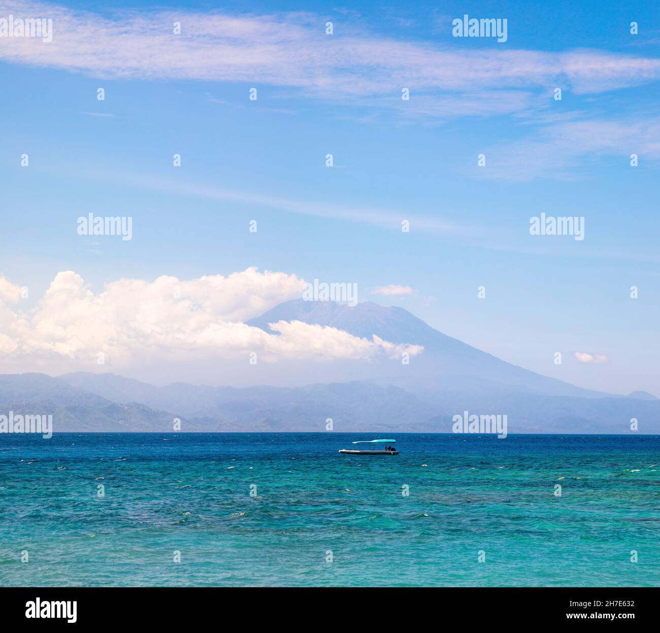 Aktiver Vulkan Mount Agung, bedeckt von Wolken in Bali Indonesien. Traditionelle Fischerboote namens Jukung am weißen Sandstrand. Hohe Wellen mit Schaum Stockfoto