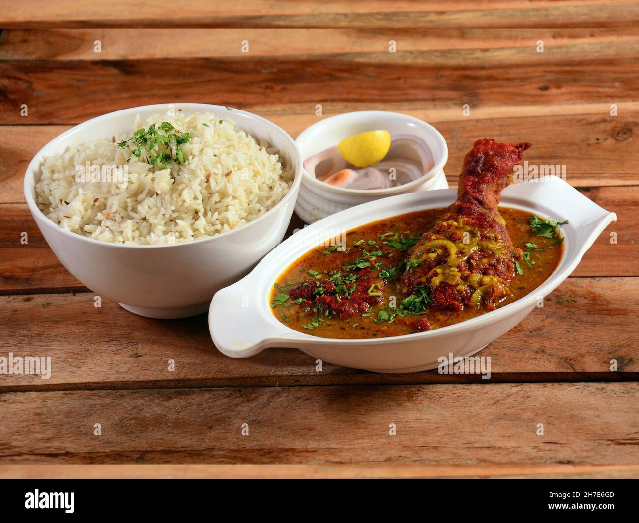 Traditionelle indische Küche, Chicken-Kerrisch und gekochter Reis auf einer weißen Keramikschüssel auf rustikalem Holzhintergrund mit Zitrone und Zwiebel Stockfoto