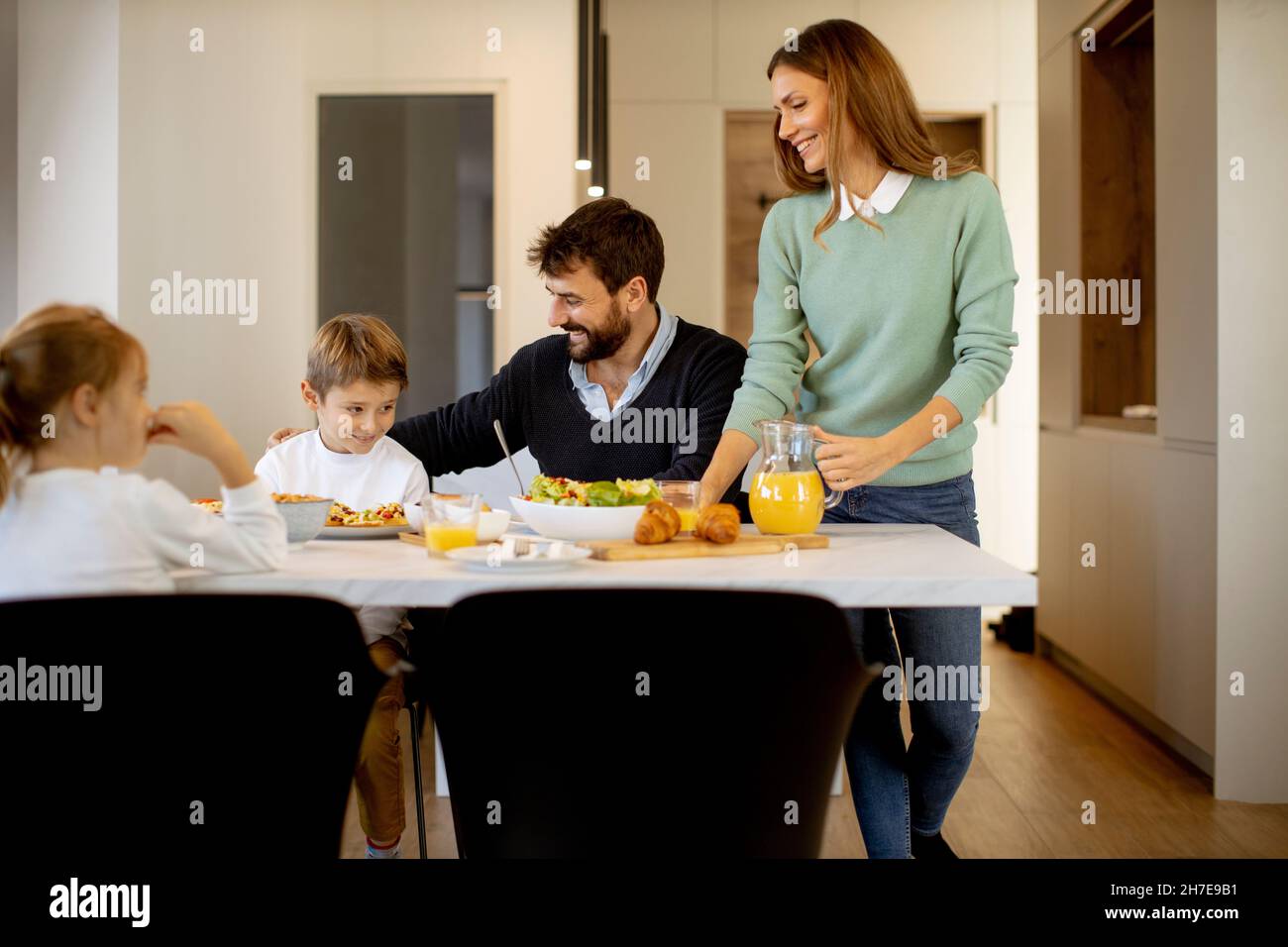 Junge glückliche Familie, die beim Frühstück am Esstisch im Apartment sprach Stockfoto