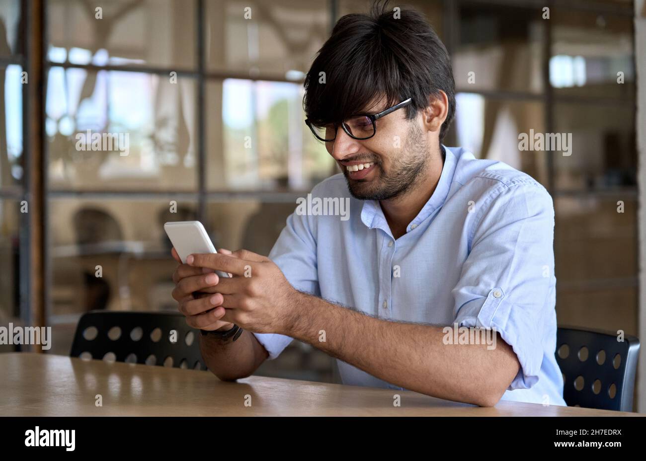 Lächelnder indischer Geschäftsmann, der Handy-Apps verwendet, die im Büro arbeiten. Stockfoto
