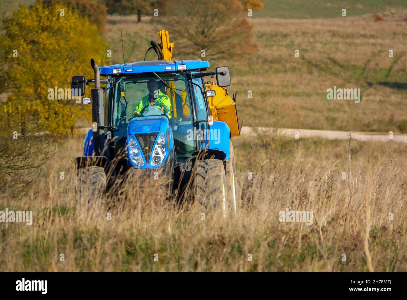 Großer blauer Traktor aus New Holland, ausgestattet mit Heckenschnitt, der durch das Land fährt, Wiltshire UK Stockfoto