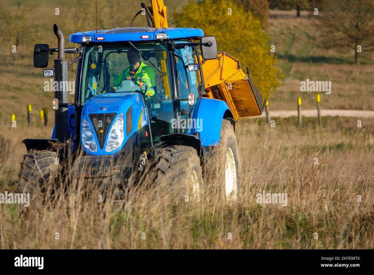 Großer blauer Traktor aus New Holland, ausgestattet mit Heckenschnitt, der durch das Land fährt, Wiltshire UK Stockfoto