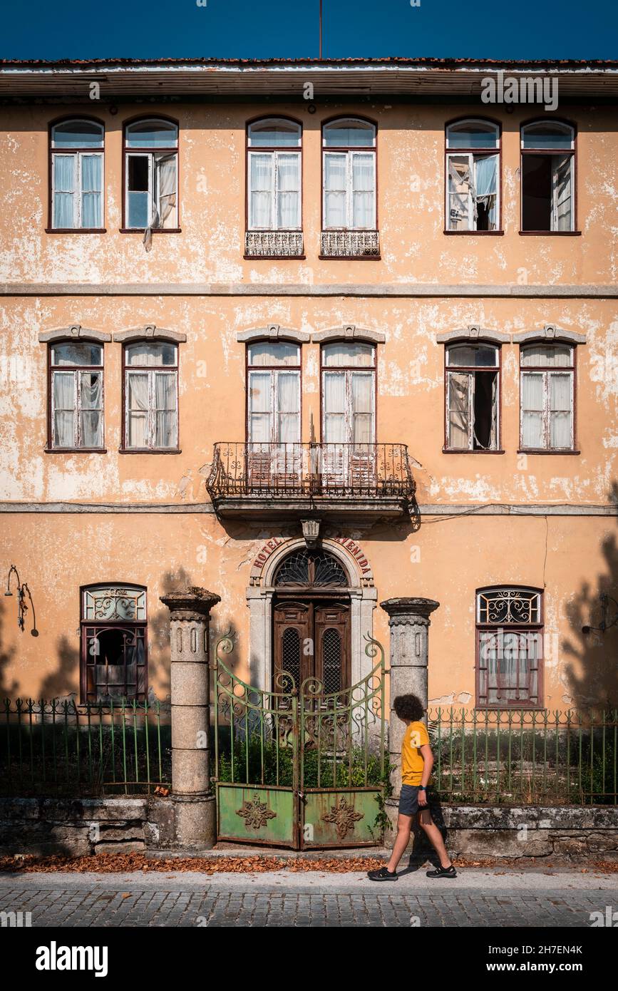 Fenster, Vordertür und Eingangzaun eines alten verlassenen Herrenhauses mit einem Jungen, der auf dem Bürgersteig vorbeikommt. Stockfoto