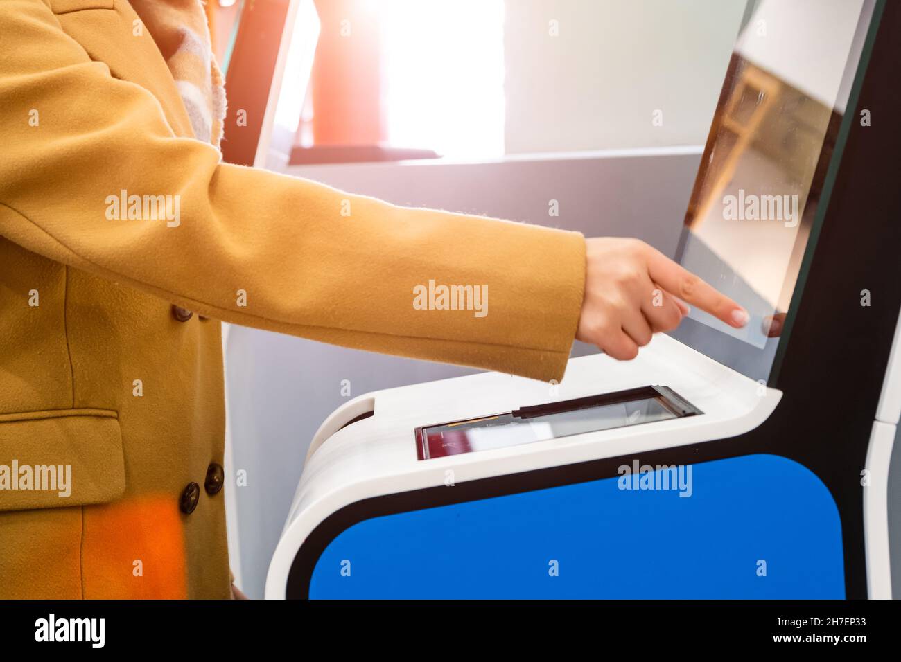 Die Passagierin nutzt einen Self-Service-Kiosk mit Touchscreen zum Check-in für den Flug, um lange Warteschlangen in der Nähe des modernen Flughafenterminals zu vermeiden Stockfoto