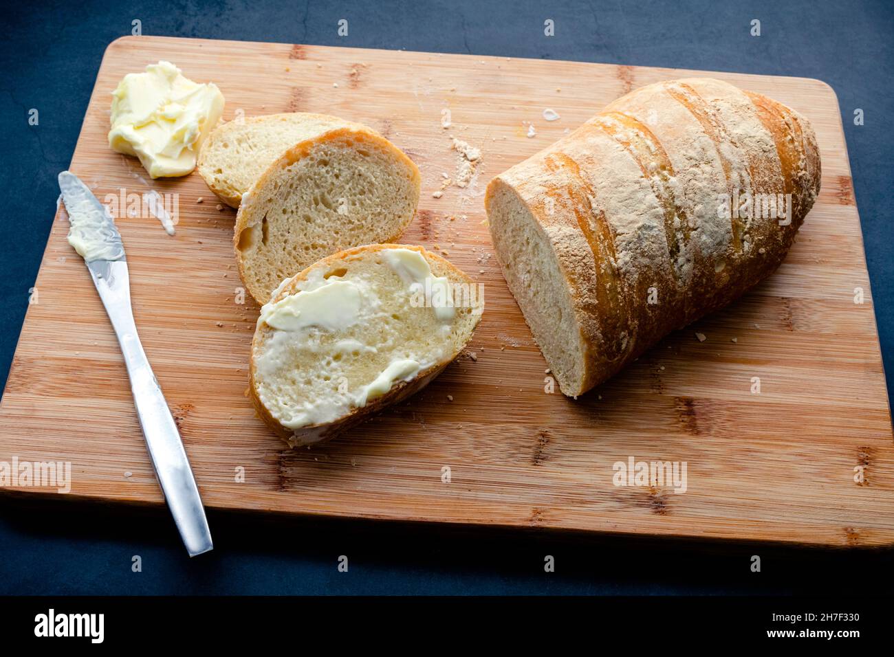 Gebutterte Baguette-Scheiben auf einem Bambus-Schneidebrett: Französisches Brot mit Butter auf einem hölzernen Schneidebrett Stockfoto