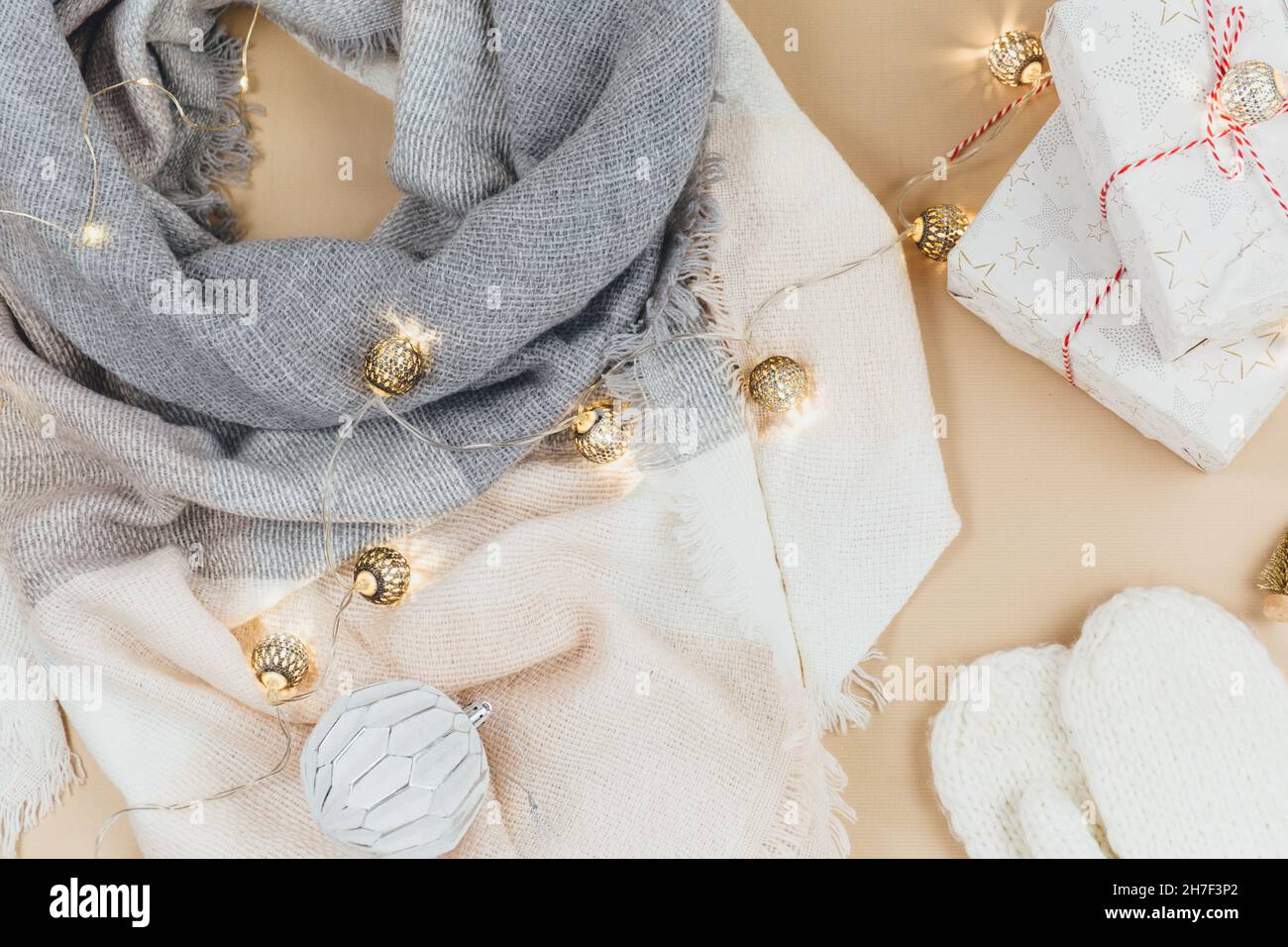 Frauen Mode Winterkleidung und Accessoires. Damen-Look mit gestricktem weißen und rosa Schal, Girlanden auf beigem pastellfarbenem Hintergrund. Stockfoto