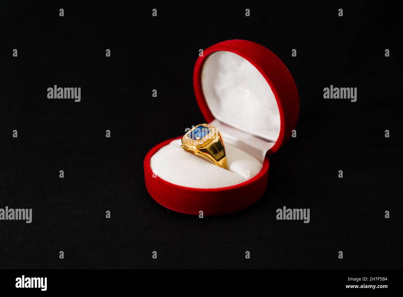 Kostbarer goldener Ring mit einem blauen Stein in der runden Schachtel,  isoliert auf schwarzem Hintergrund Stockfotografie - Alamy