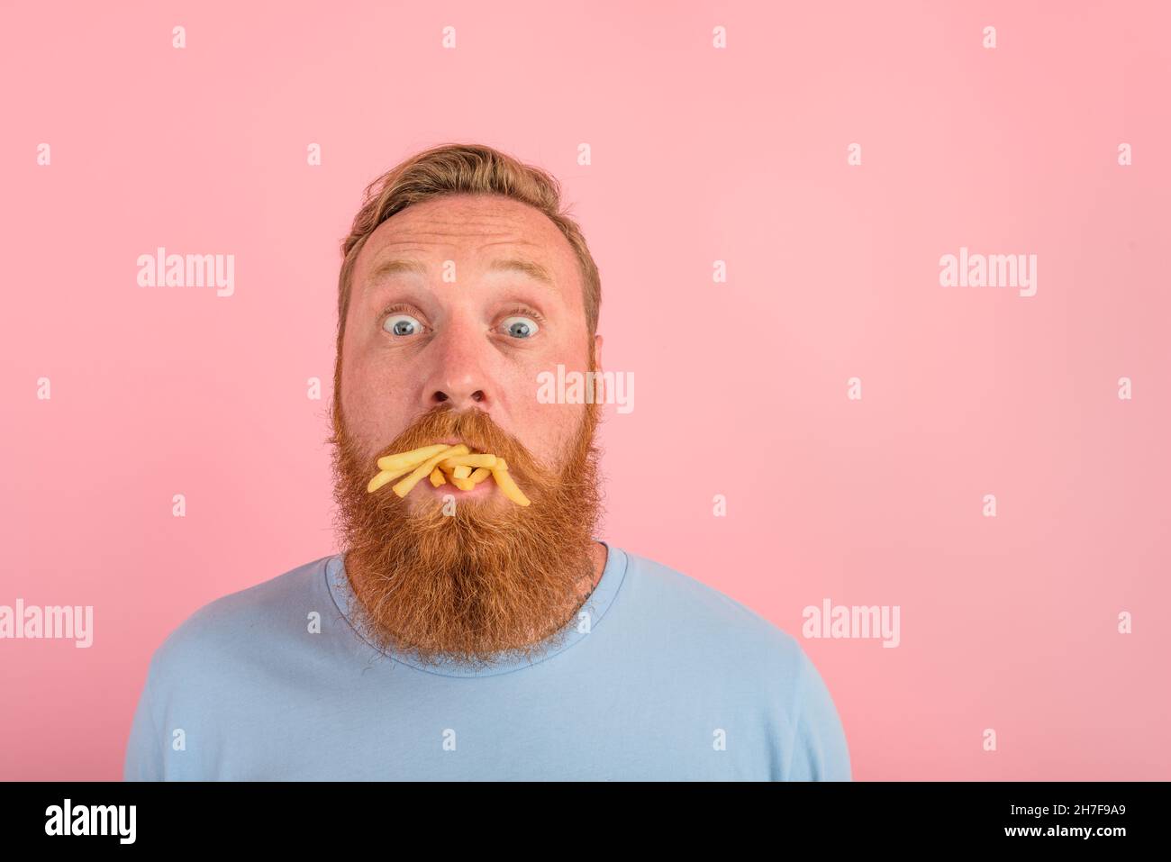 Hungriger Mann mit Bart und Tattoos frisst ein Sandwich mit Hamburger und Kartoffeln Stockfoto