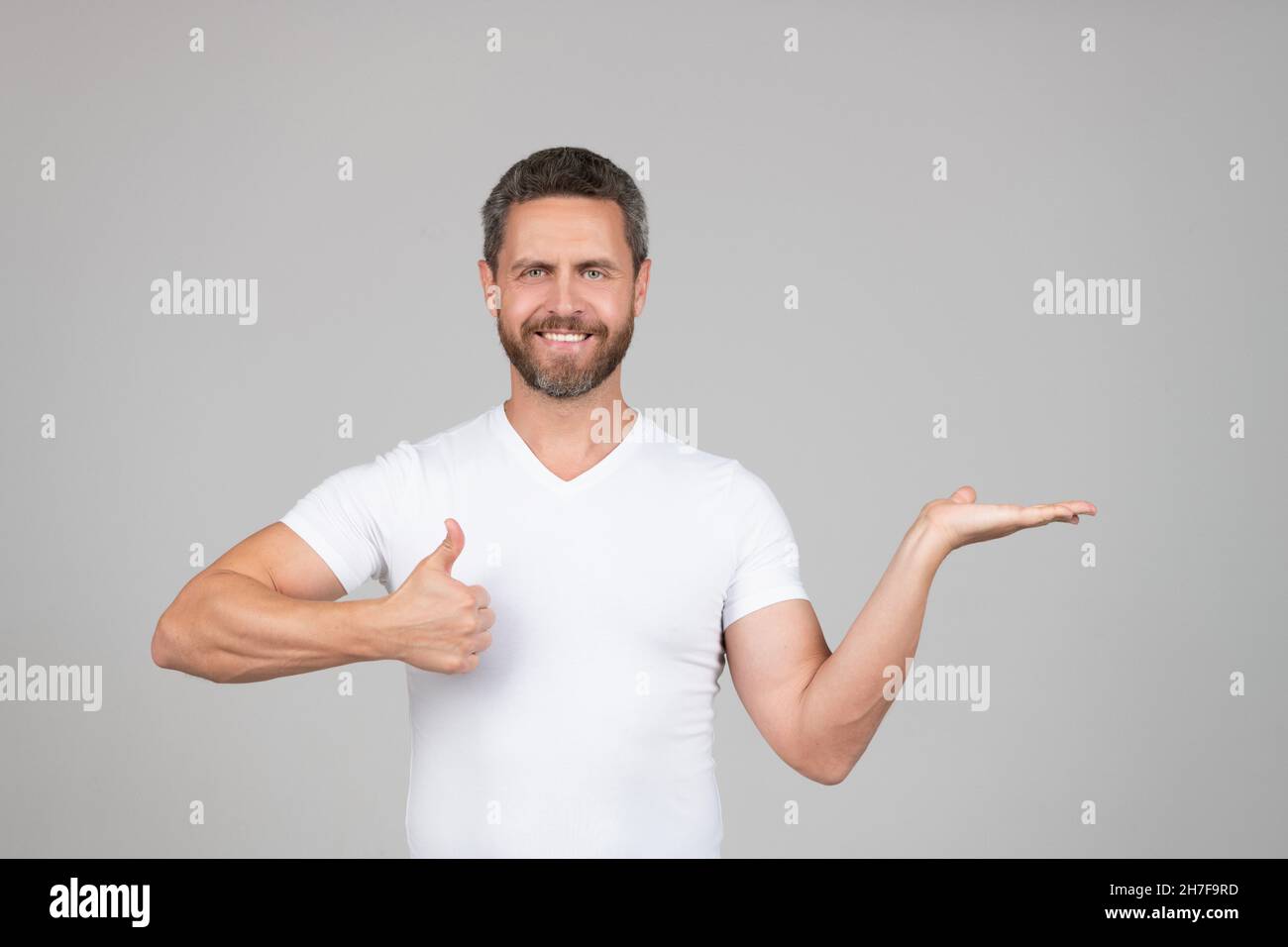Das beste Produkt präsentieren. Glücklicher Mann zeigt die offene Hand und zeigt den Daumen nach oben. Produktpräsentation Stockfoto