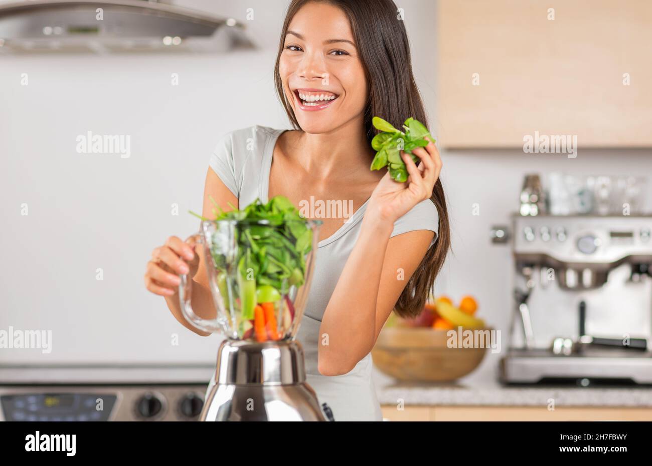 Gesunde grüne Smoothie Asiatische Frau mit Spinat im Mixer zu entgiften Gemüsesaft zu Hause zu machen. Lächelnde junge Frau beim Kochen Stockfoto