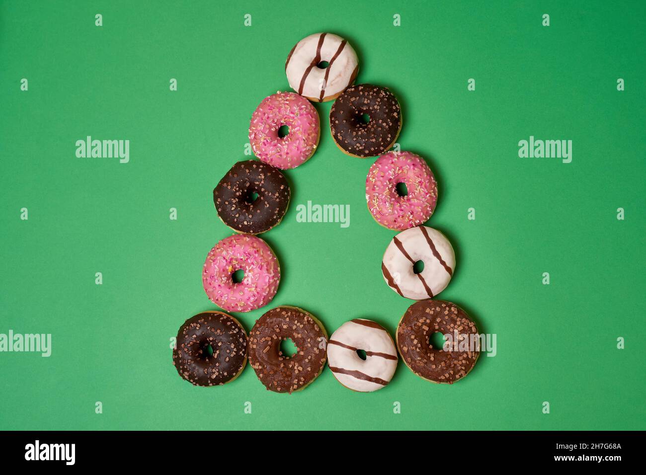 Donuts rosa, braun und weiß in Dreiecksform auf grünem Hintergrund Stockfoto