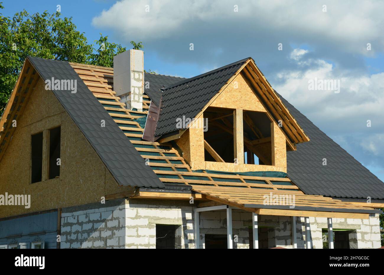 Dachkonstruktion im Dachgeschoss. Eine Nahaufnahme eines Holzdachs, das über einer Dampfsperre und einer Metalldachziegel-Installation rahmte, Dachfenster, Schornsteinkonstruktion Stockfoto