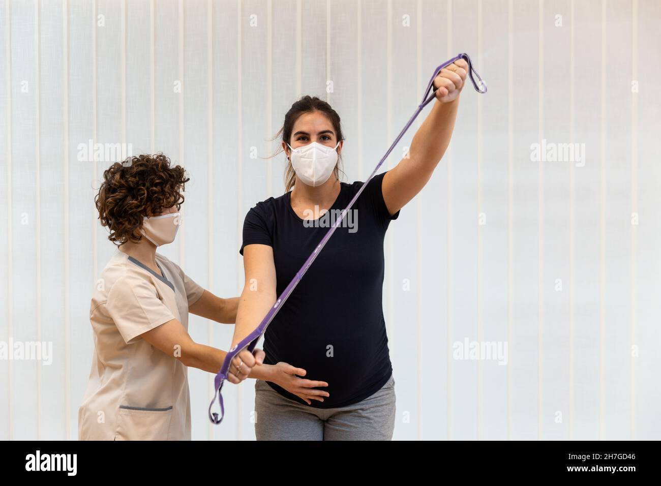 Eine Schwangerin, die mit Hilfe eines Physiotherapeuten mit einem Gummiband trainiert Stockfoto