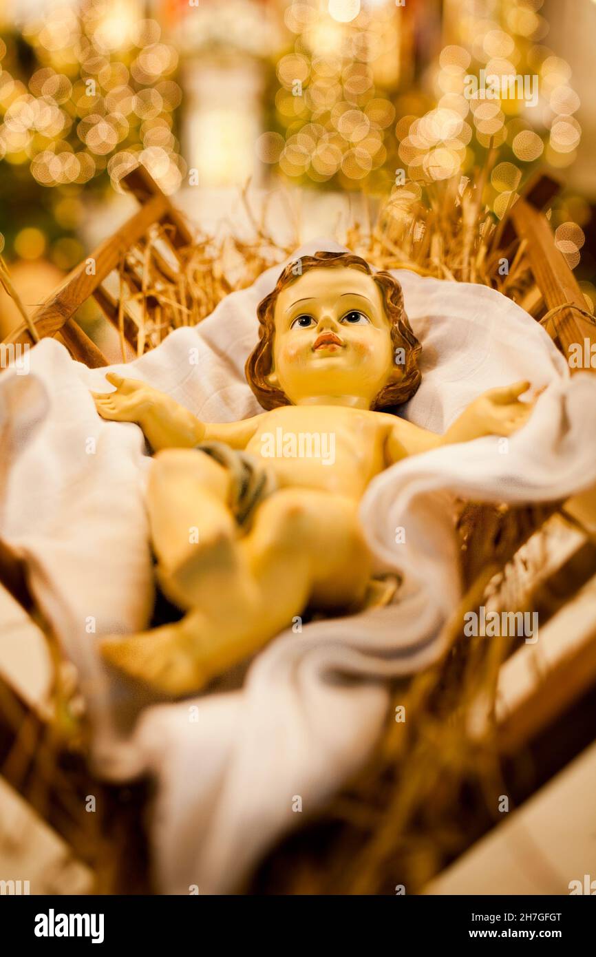 Jesuskind in der Krippe, Weihnachtslicht auf den Bäumen im Hintergrund, künstlerische Fotografie, Fotos über dem weihnachtsbaum mit Blick in die Kirche Stockfoto